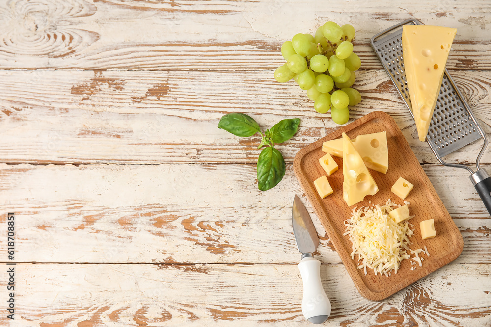 Board with tasty Swiss cheese and grapes on light wooden background