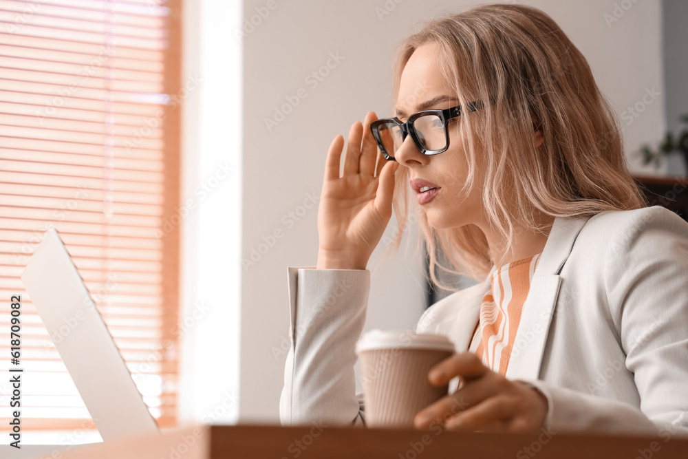 Young businesswoman with stylish eyeglasses and cup of coffee in office