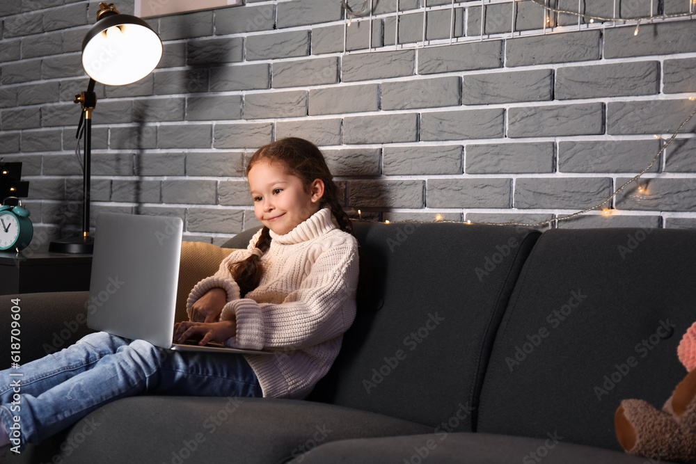 Little girl with laptop doing lessons at home late in evening