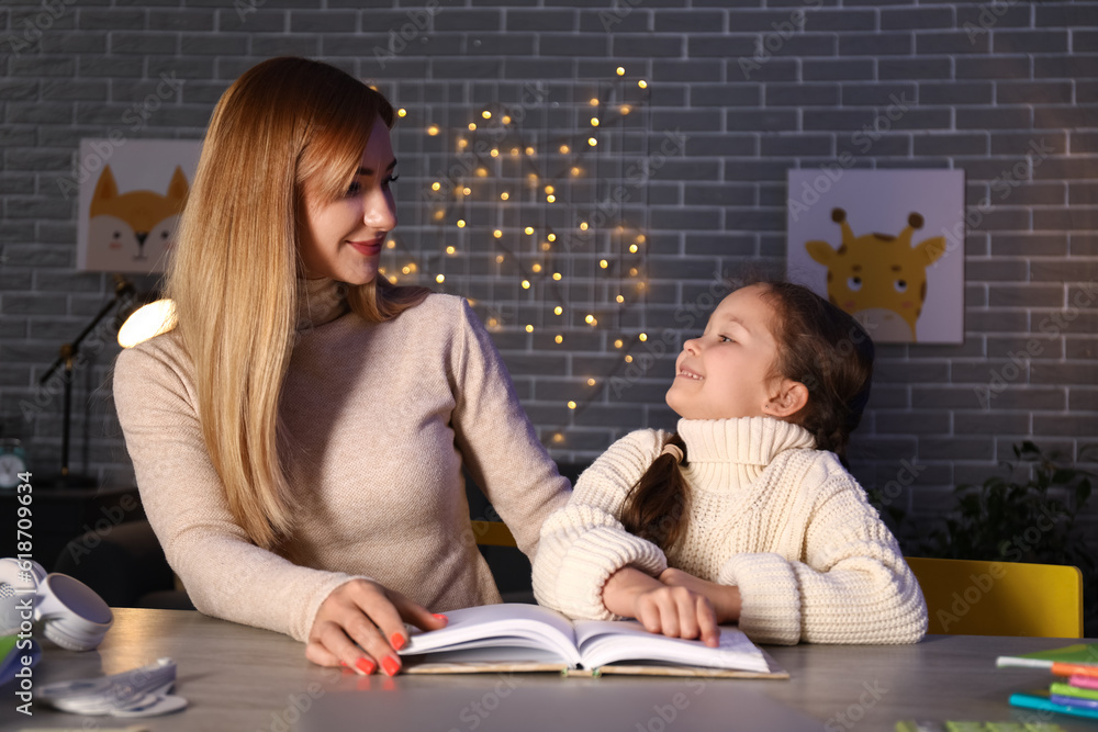 Little girl with her mother doing lessons at home late in evening