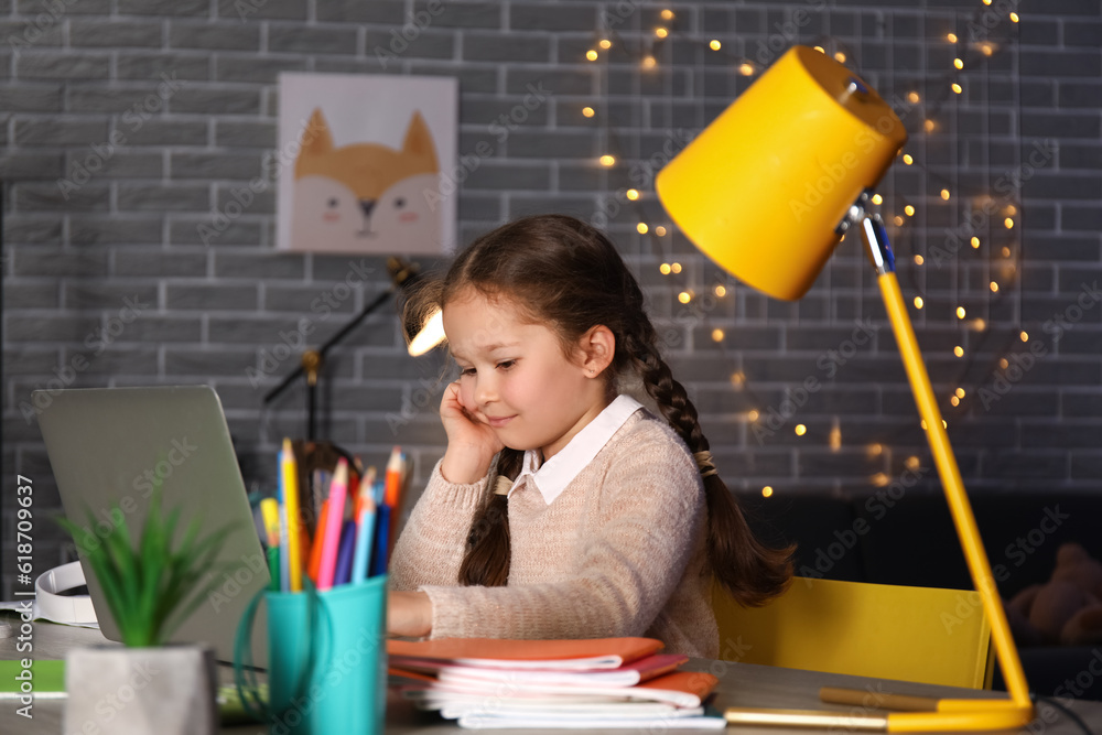 Little girl with laptop doing lessons at home late in evening