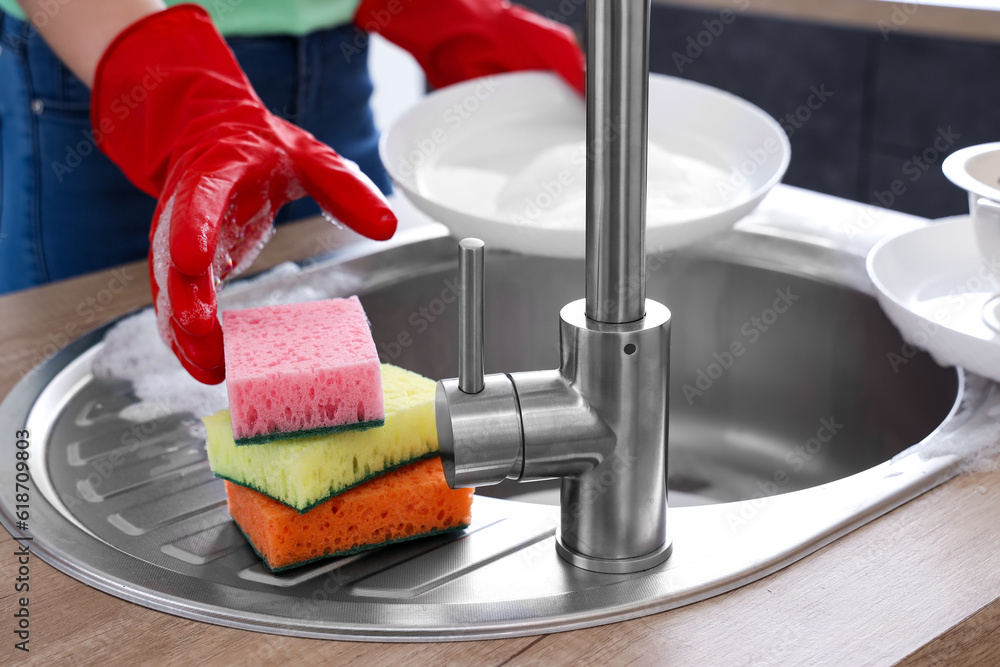 Woman in red rubber gloves washing dishes with sponge