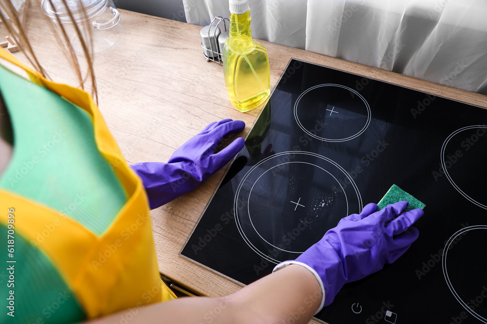 Woman in purple rubber gloves cleaning electric stove with sponge