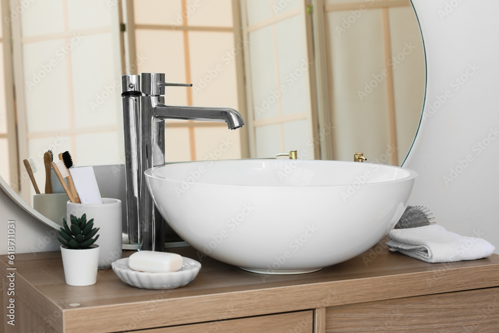 Sink bowl, cup with toothbrushes, soap bar and houseplant on wooden cabinet in bathroom