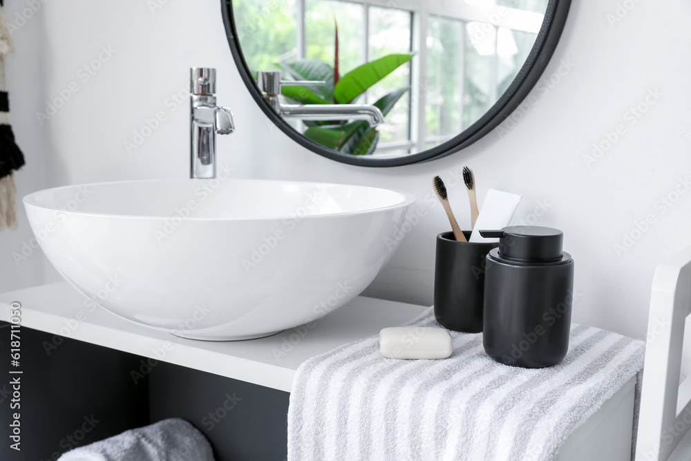 Sink bowl, soap bar, towel and cup with toothbrushes on shelving unit in bathroom