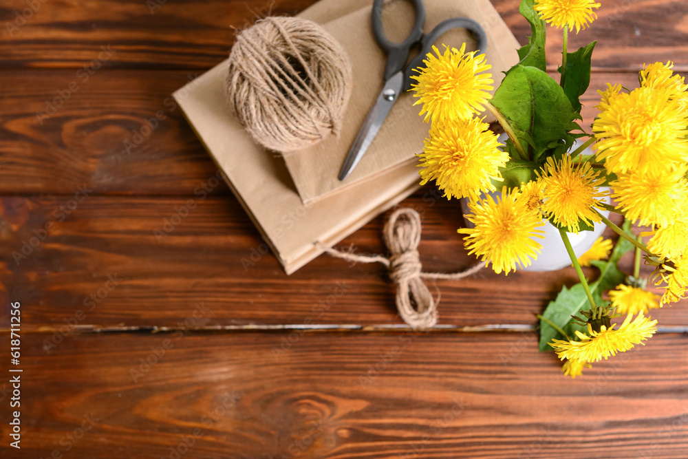 Vase with yellow dandelion flowers, books, rope and scissors on wooden background