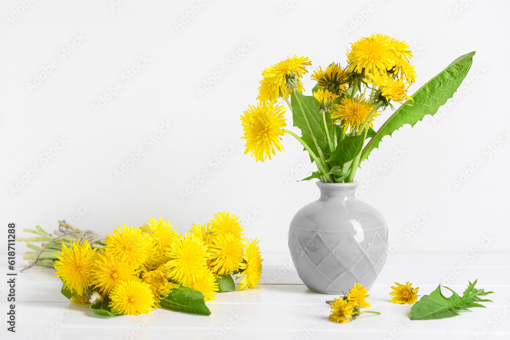 Vase with beautiful dandelion flowers on table near light wall