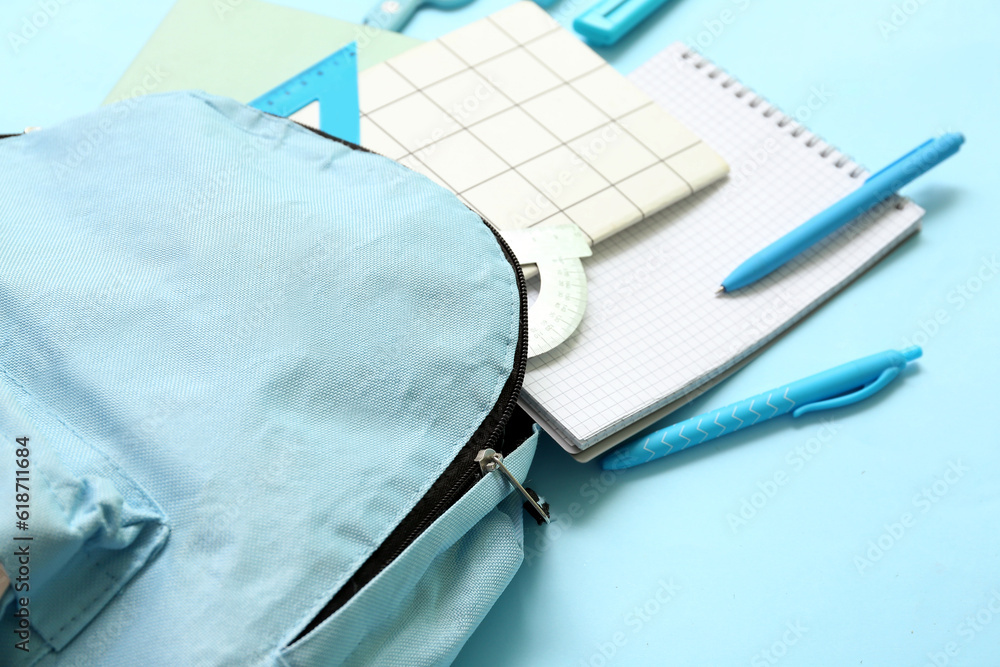 School backpack with different stationery on blue background, closeup