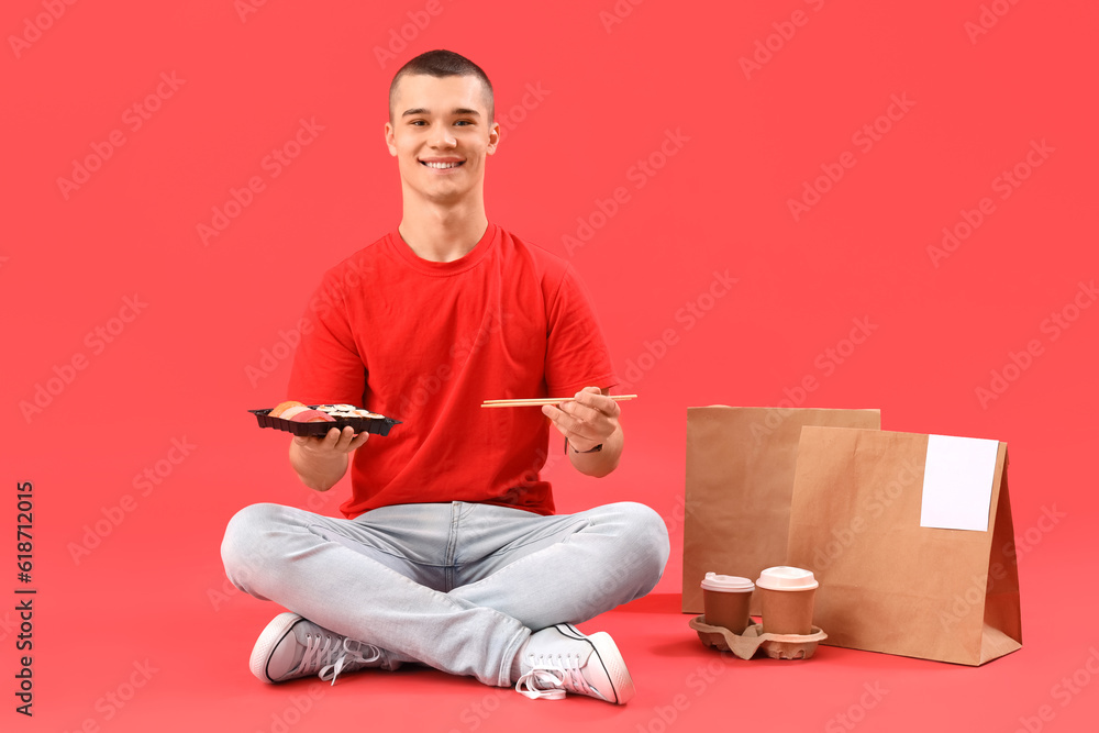 Young man eating tasty sushi on red background