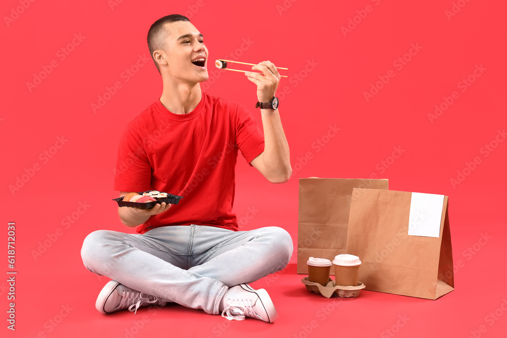 Young man eating tasty sushi on red background