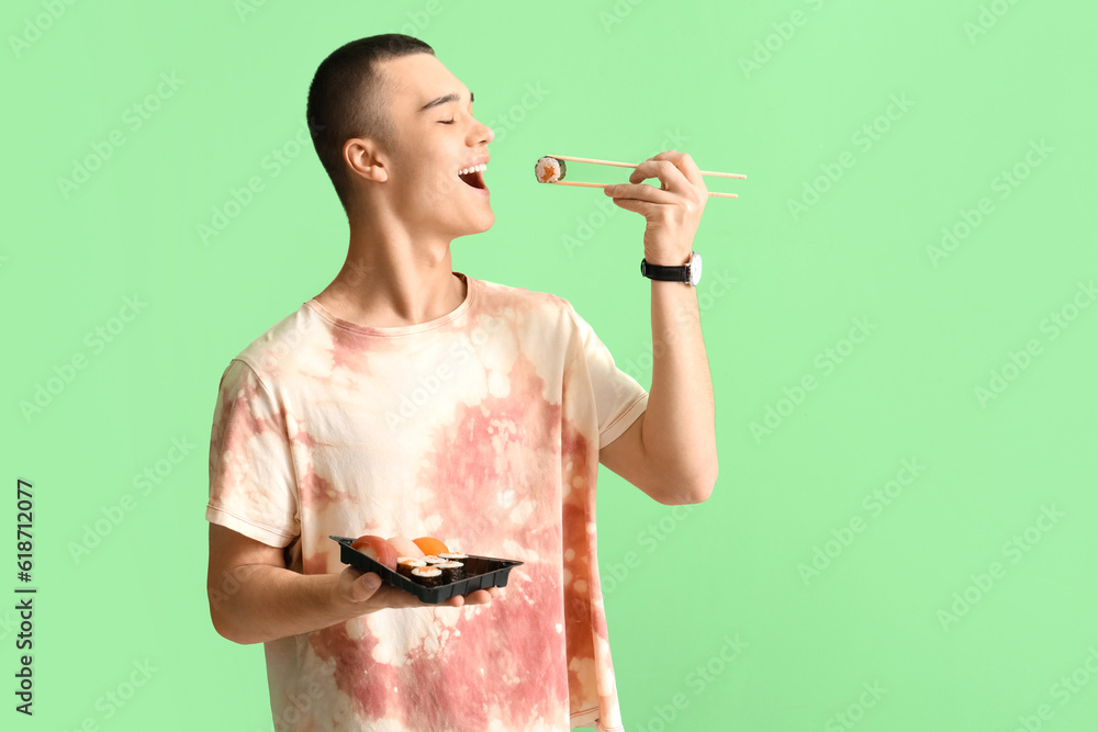 Young man eating tasty sushi on green background