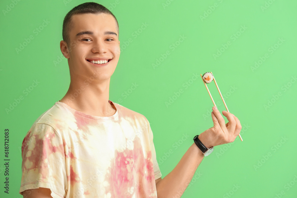 Young man with tasty sushi roll on green background