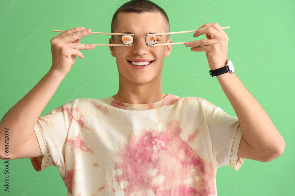 Funny young man with tasty sushi rolls on green background