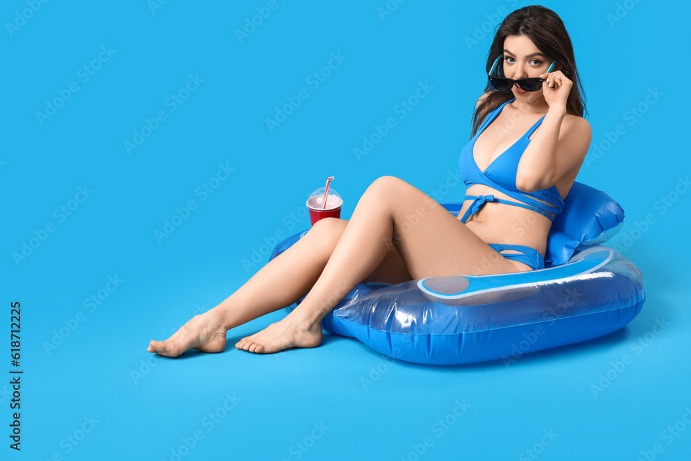 Young woman in sunglasses with swim ring on blue background