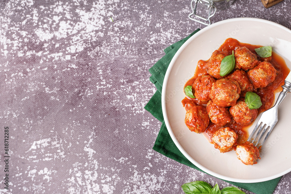 Plate of tasty meat balls with tomato sauce and basil on grey background