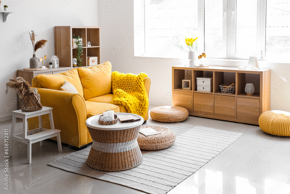 Interior of light living room with stylish yellow sofa, coffee table and wicker poufs