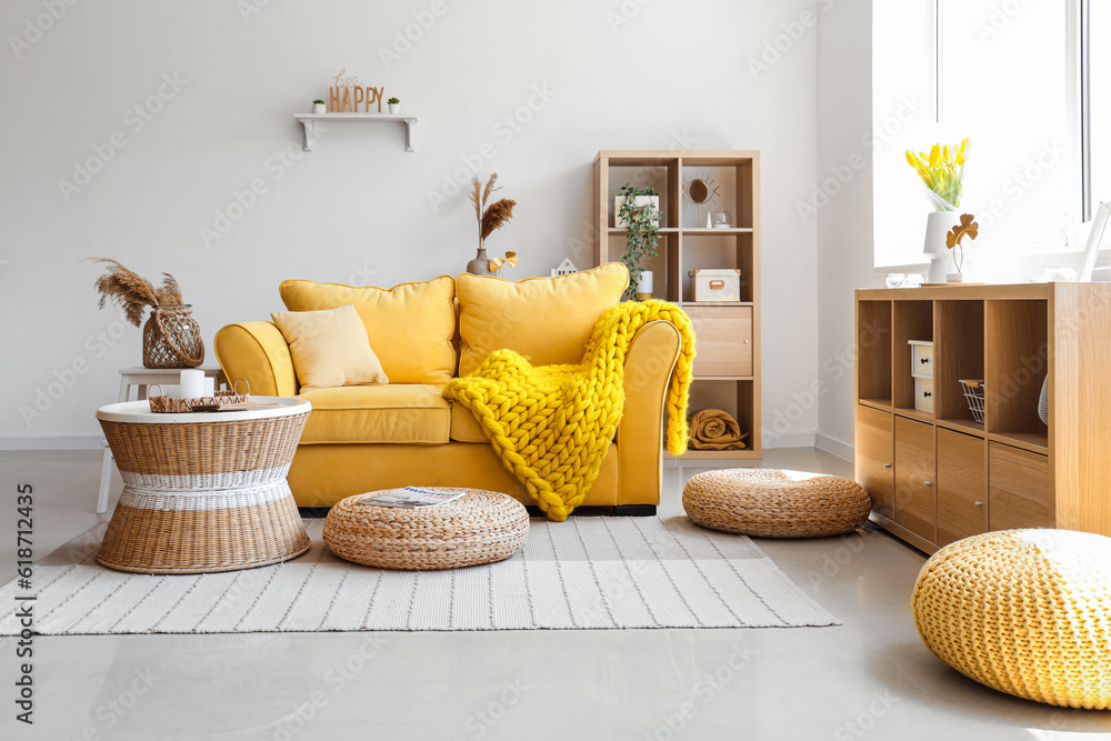 Interior of light living room with stylish yellow sofa, coffee table and wicker poufs