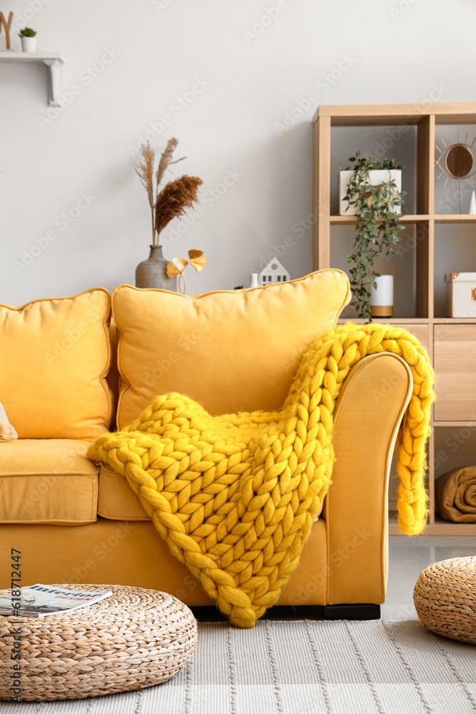 Stylish yellows sofa with soft blanket in interior of light living room