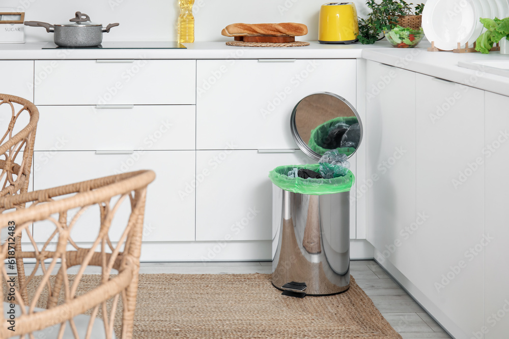 Opened trash bin with garbage in interior of light kitchen