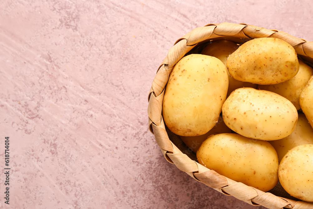 Wicker basket with raw baby potatoes on pink background