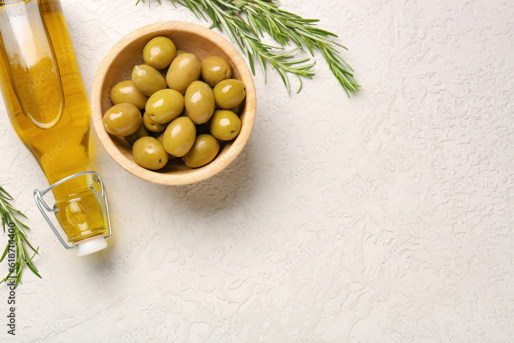 Bowl with ripe olives and bottle of oil on light background