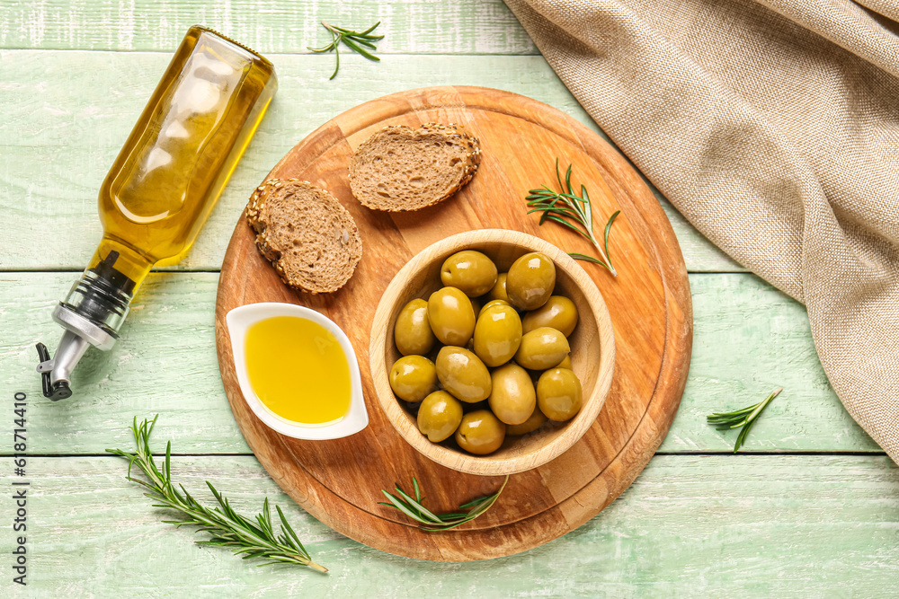 Ripe olives, bread, bowls and bottle of oil on green wooden background