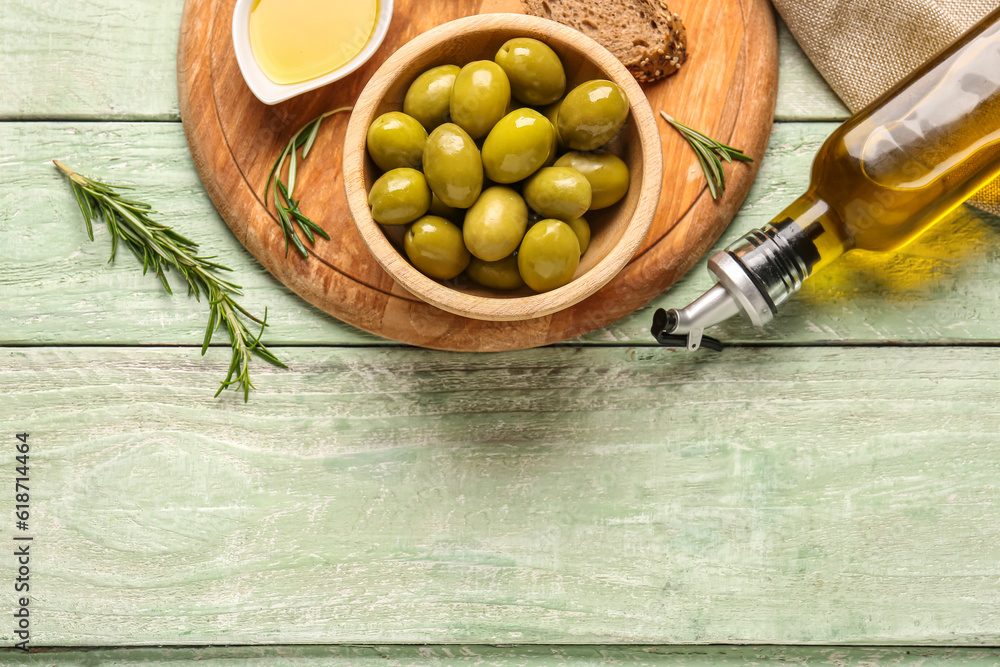 Bowl with ripe olives and bottle of oil on green wooden background