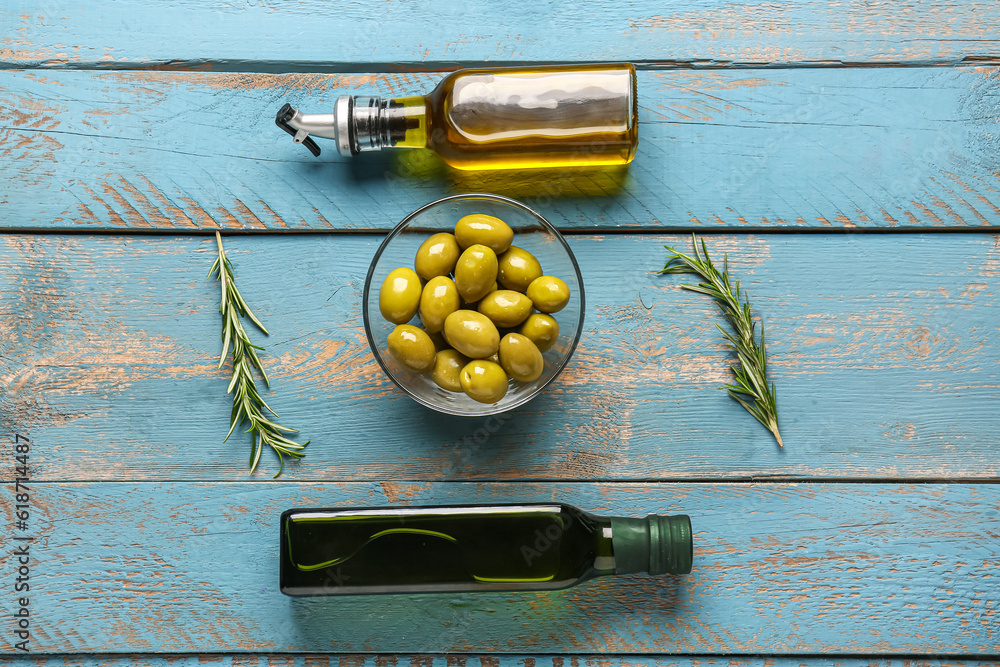 Bowl with ripe olives and bottles of oil on blue wooden background