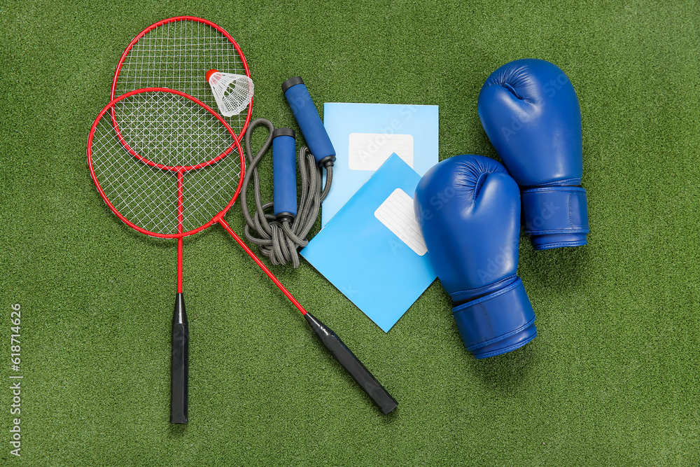 Notebooks with boxing gloves, badminton rackets and skipping rope on color background