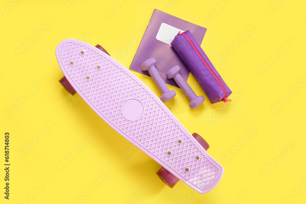 Skateboard with dumbbells, pencil case and notebook on yellow background