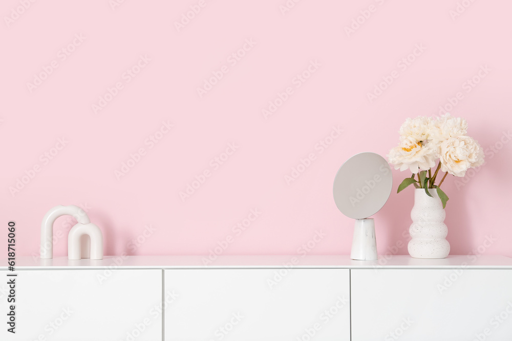 Vase of white peonies and mirror on dresser near pink wall