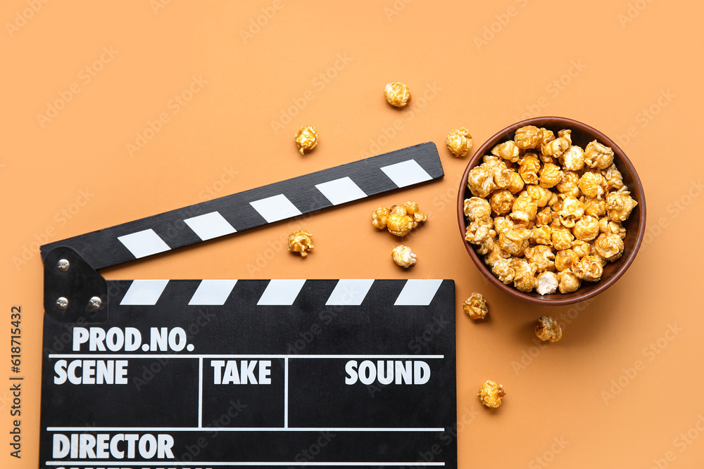 Bowl with tasty popcorn and clapperboard on brown background