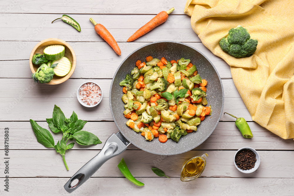 Frying pan with different vegetables on light wooden background