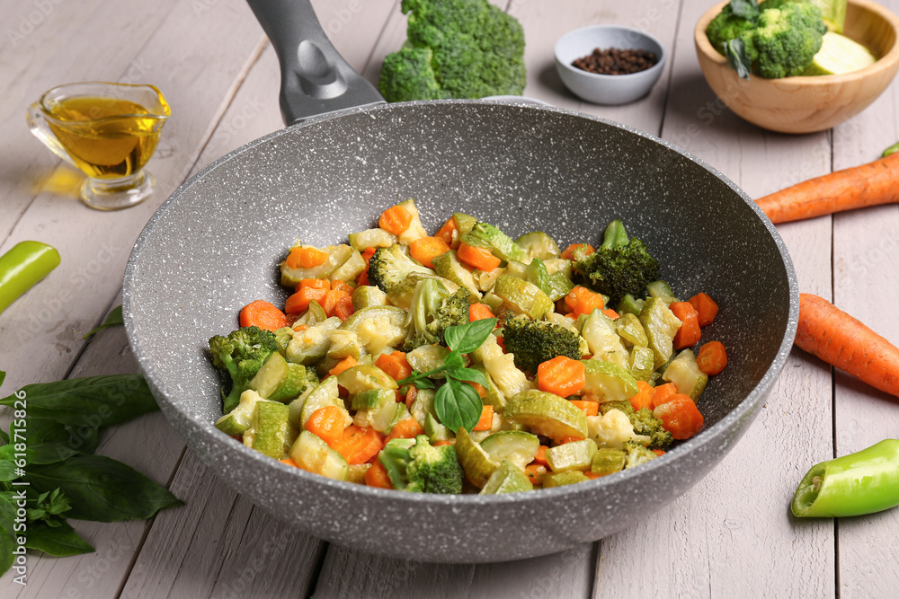 Frying pan with different vegetables on light wooden background