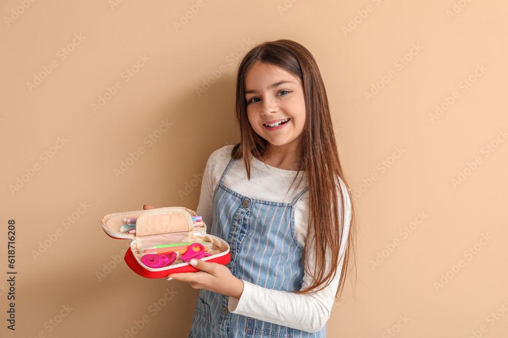 Little girl with pencil case on beige background