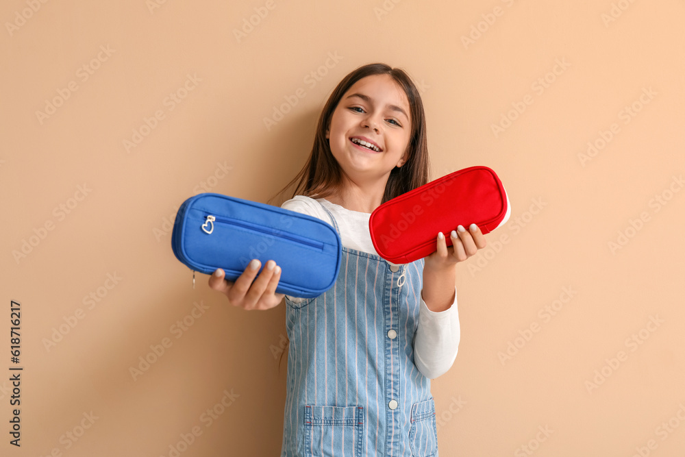 Little girl with pencil cases on beige background