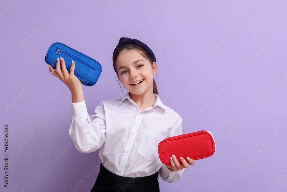 Little schoolgirl with pencil cases on lilac background