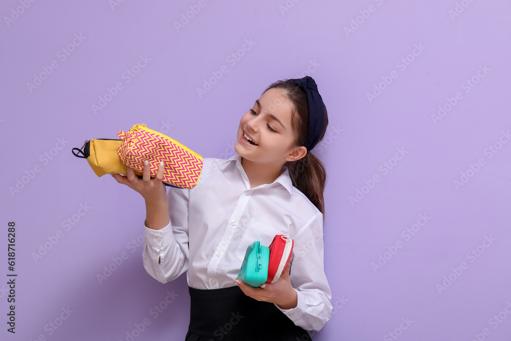 Little schoolgirl with pencil cases on lilac background