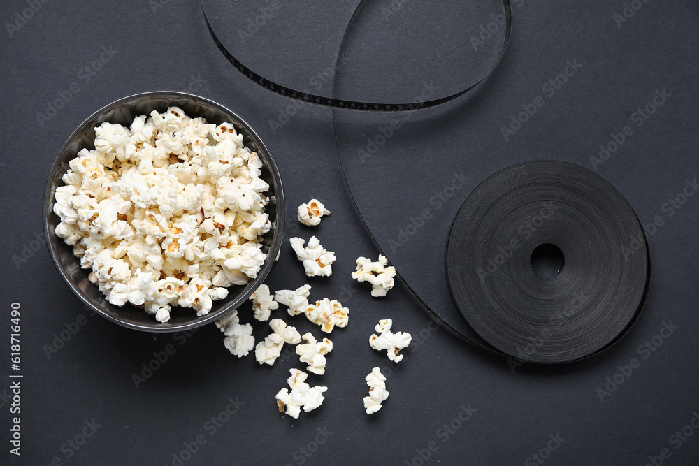 Bowl with tasty popcorn and film reel on black background