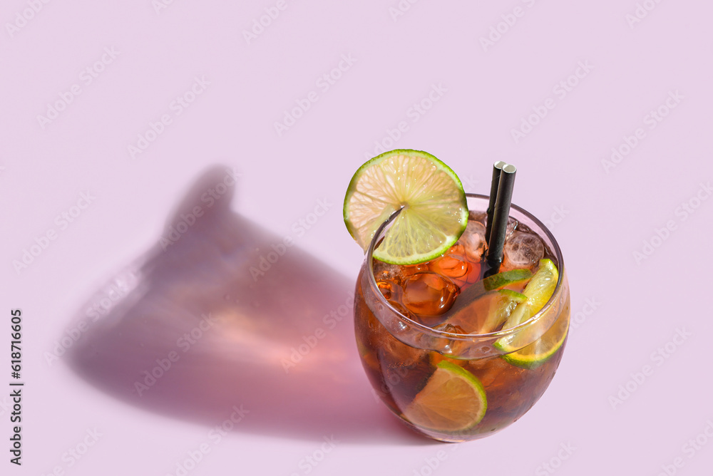 Glass of cold Cuba Libre cocktail on lilac background