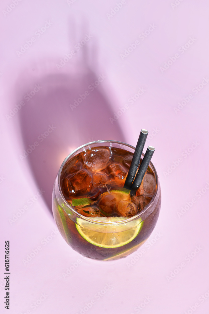 Glass of cold Cuba Libre cocktail on lilac background