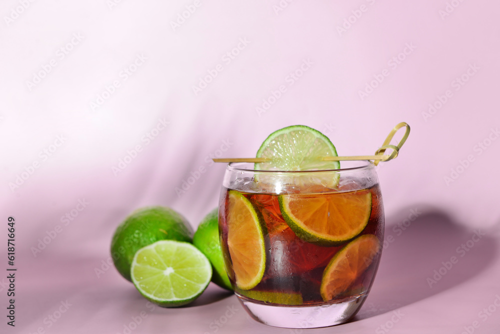 Glass of cold Cuba Libre cocktail on lilac background