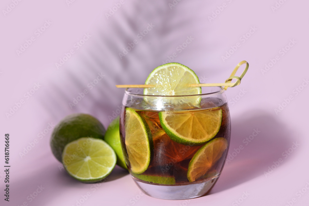 Glass of cold Cuba Libre cocktail on lilac background