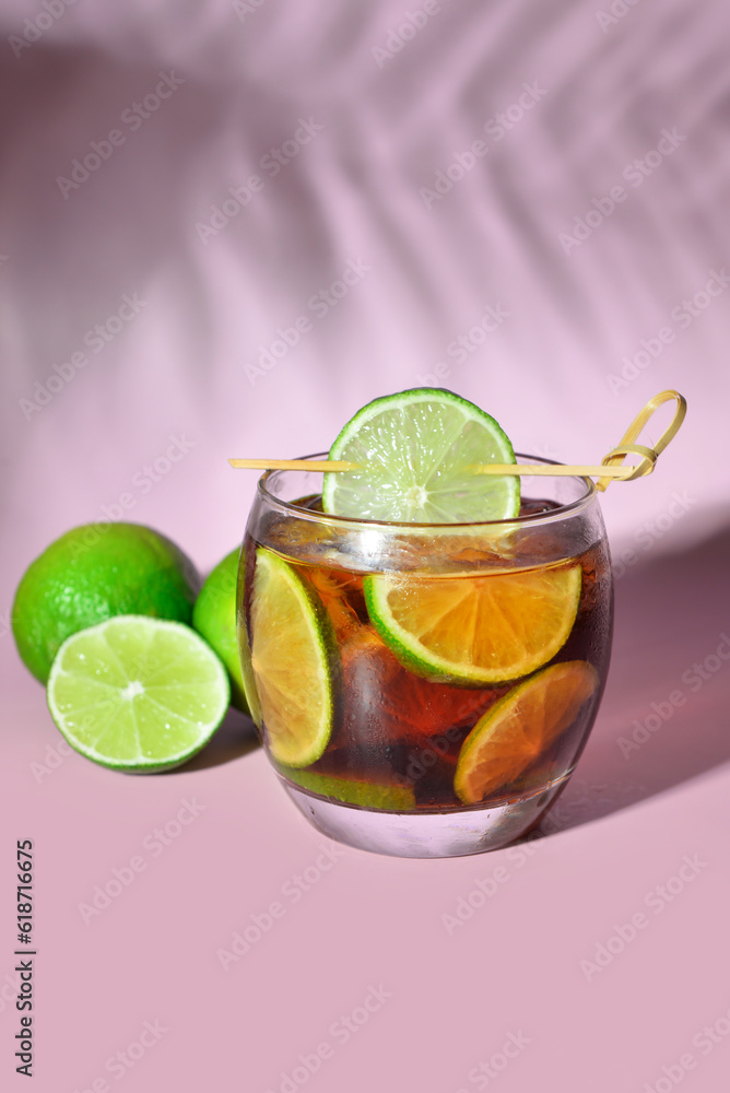 Glass of cold Cuba Libre cocktail on lilac background