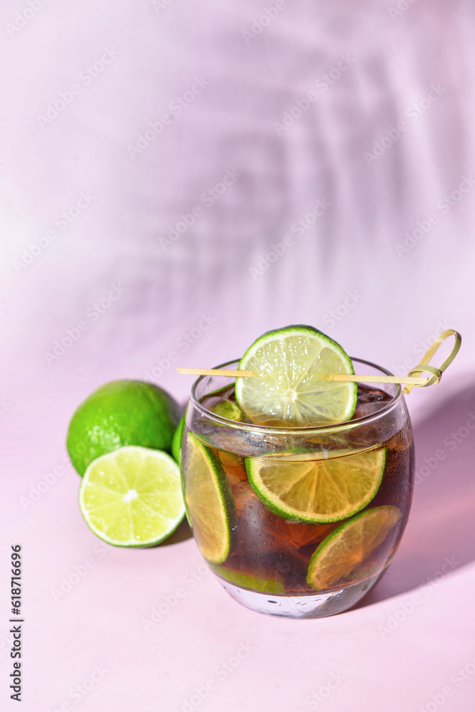 Glass of cold Cuba Libre cocktail on lilac background