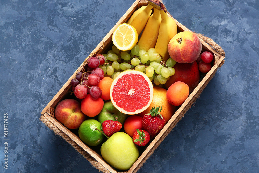 Wooden box with different fresh fruits on blue background