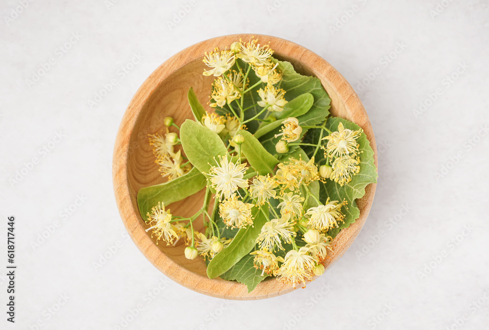 Wooden bowl with fresh linden flowers on light background