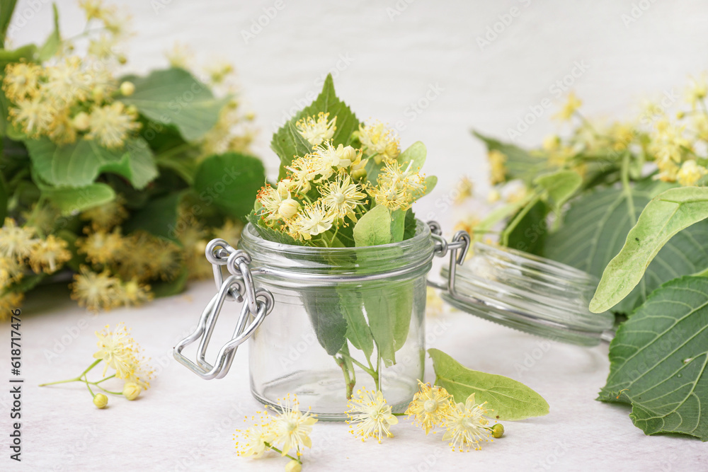 Glass jar with fresh linden flowers on light background