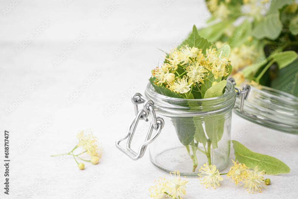 Glass jar with fresh linden flowers on light background