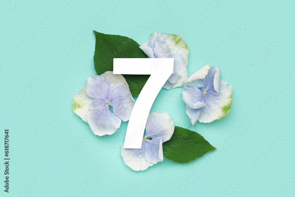 Green leaves and flowers with paper number seven on turquoise background